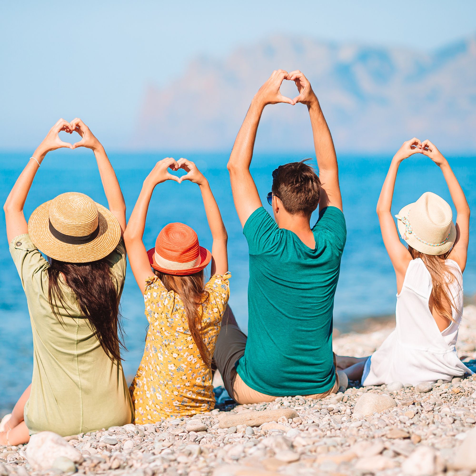 Friends holding sun hats overhead on a sunny beach